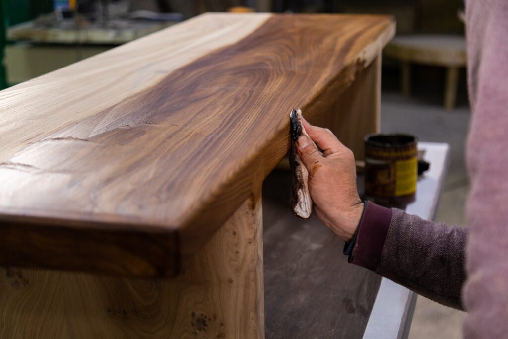 A carpenter applies a shiny finish to wood.