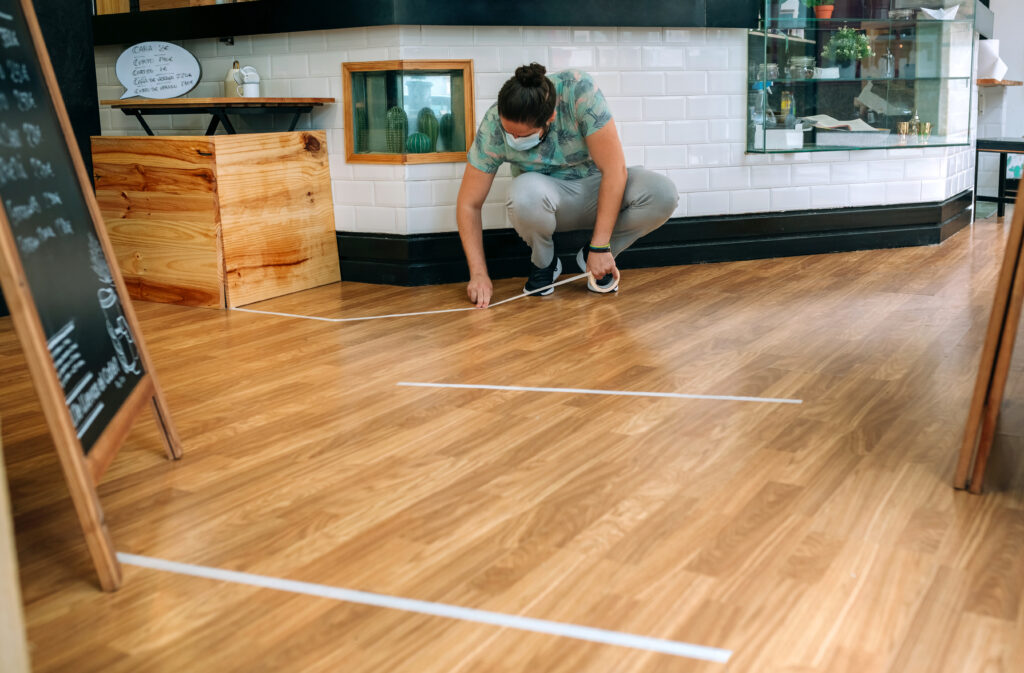 A man applies a lacquer finish on a patterned hardwood floor.
