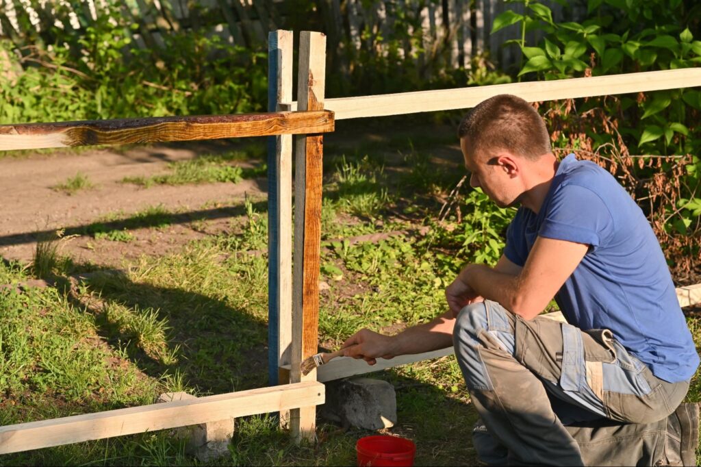  A man brushes wood stain onto a fence.