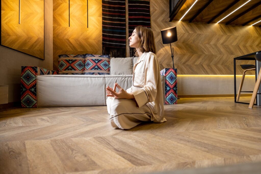 A woman calmly meditating on a hardwood floor.