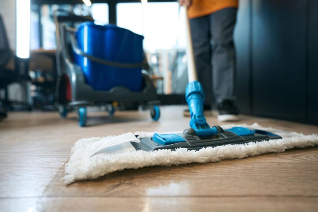 A man cleaning a hardwood floor with a mop and bucket.