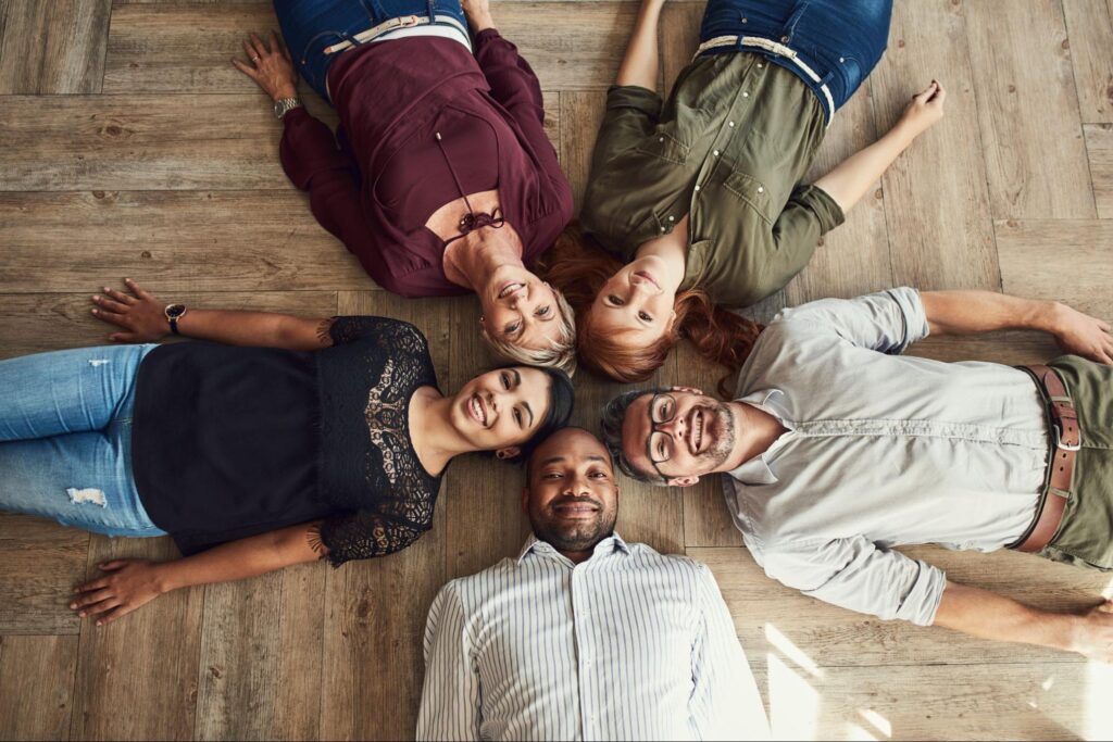 High angle photo of friends laying down on a hardwood floor.