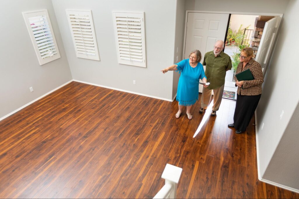 A real estate agent shows a home with a hardwood floor to an elderly couple.
