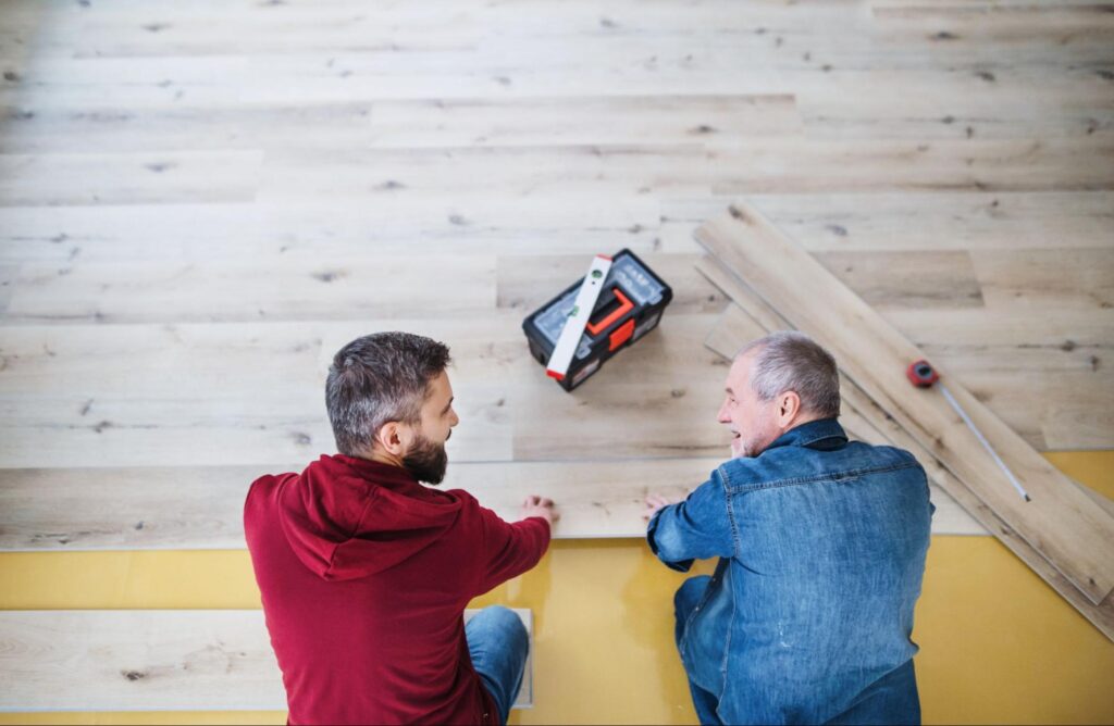 Two men installing flooring next to a tool box. 