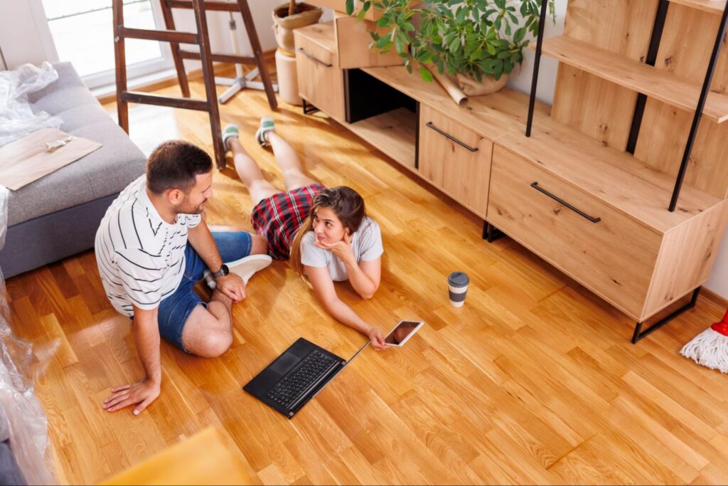 Couple sitting on a wood floor using laptops and cell phones. 